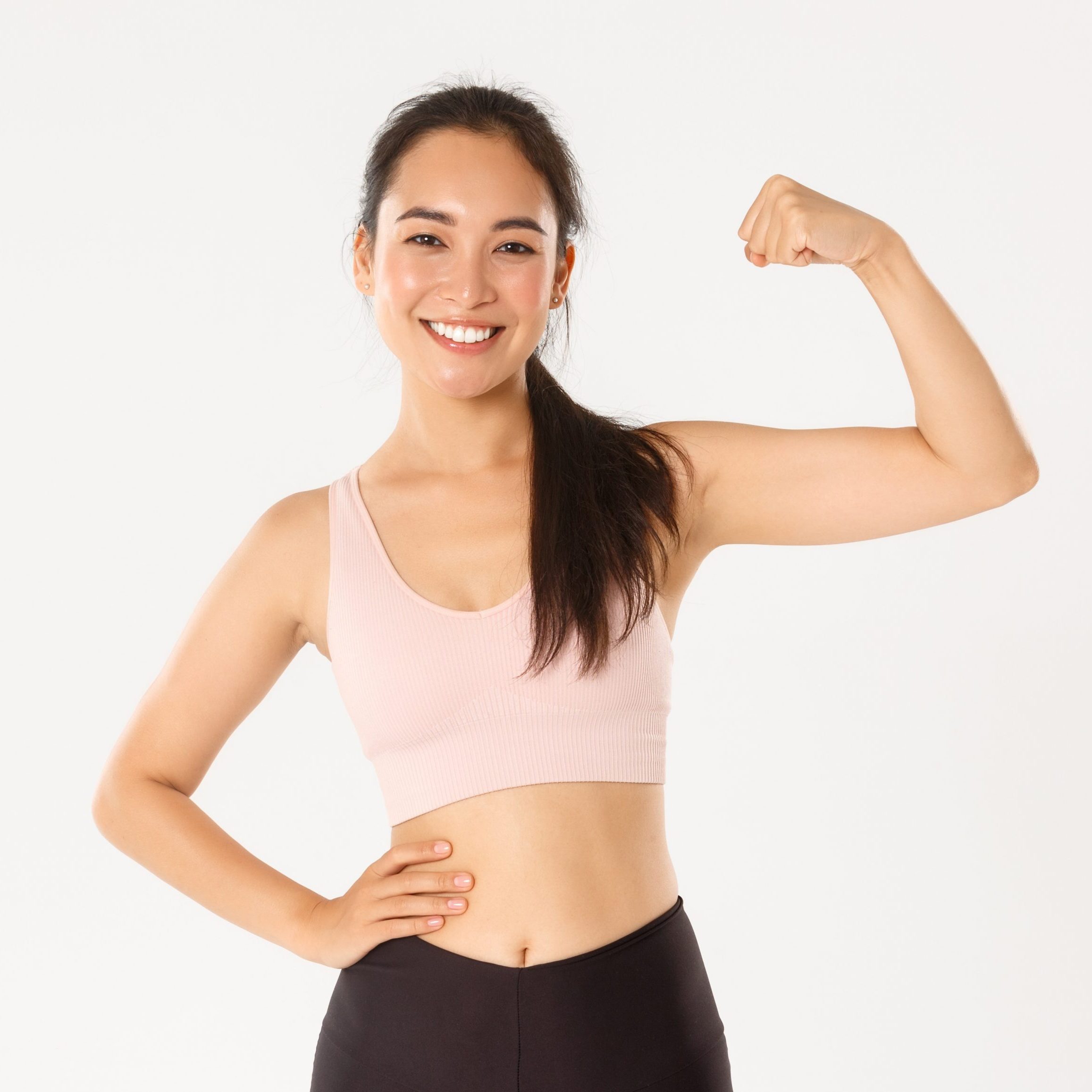 Sport, wellbeing and active lifestyle concept. Portrait of smiling slim and strong asian fitness girl, personal workout trainer showing muscles, flexing biceps and look proud, white background.